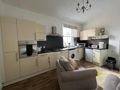 a kitchen with white cabinets and a couch in a room at Stylish 2nd Floor Georgian 1 Bedroom Apartment in Dumfries