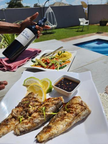 una mesa con un plato de pescado y una botella de vino en Minnestay Guest House, en Palapye