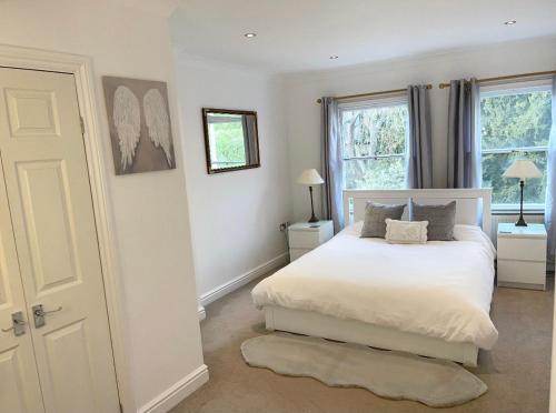 a bedroom with a white bed and two windows at WATCH CHANGING OF THE GUARD AND WALK TO THE CASTLE! 2 Bedroom Apartment in Windsor