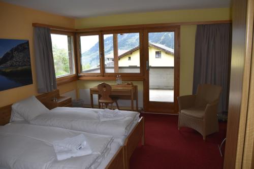 a hotel room with two beds and a desk and window at Hotel Pazzola in Disentis