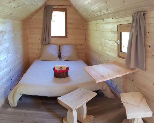 a bed in a wooden cabin with a table and benches at LE NOYER DU BARON in Le Lauzet-Ubaye