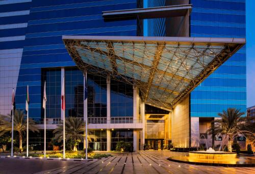 un bâtiment avec une façade en verre et des palmiers devant dans l'établissement The H Dubai, à Dubaï