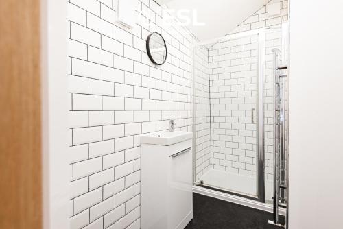 La salle de bains est pourvue de carrelage blanc, d'un lavabo et d'une douche. dans l'établissement Sunnyside, Henblas Road, Wrexham, 