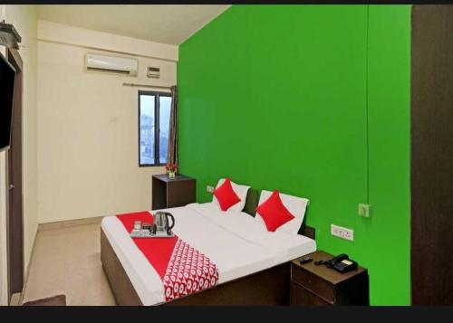 a green walled bedroom with a bed with red pillows at Flagship Hotel Heaven in Patna