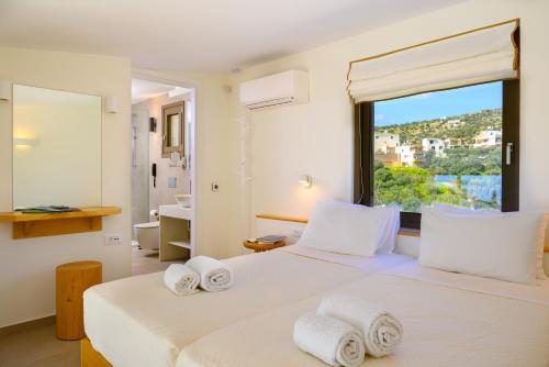a white bedroom with two beds and a window at Mirabella Hills in Agios Nikolaos