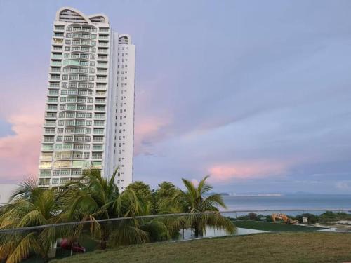 a tall white building with palm trees and the ocean at Southbay Seaview Condo A10 #10minQueensbay #15minSPICE in Bayan Lepas