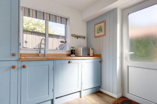a kitchen with white cabinets and a sink and a window at Egret in South Creake
