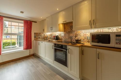 a kitchen with white cabinets and a microwave and a window at Hollyhocks in Docking