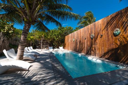 a swimming pool with chairs and a fence and a palm tree at Kai Tulum in Tulum