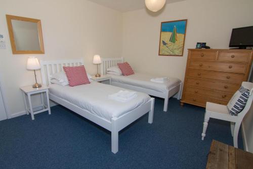 a bedroom with two beds and a dresser and a chair at Sea Aster in Brancaster