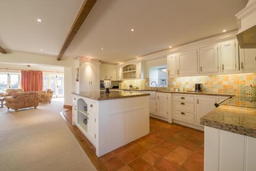 a large kitchen with white cabinets and a living room at Geddings Farm Barn in Ringstead