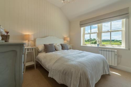 een witte slaapkamer met een bed en een raam bij Sea Holly Cottage in Thornham