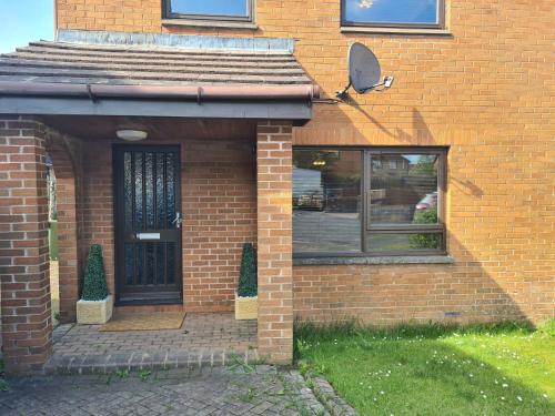 a brick house with a black door and a window at 3 BEDROOM HOUSE WITH FREE PARKING - Travel Host in Nitshill
