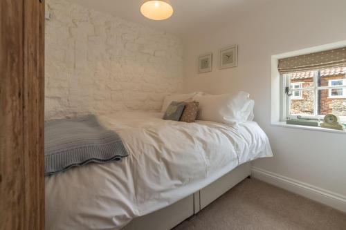 a bedroom with a bed with white sheets and a window at Sextons Yard Cottage in Docking