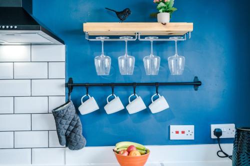 a kitchen with a blue wall with cups and a bowl of fruit at Talbot House in Chester