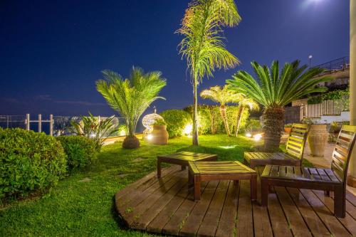 a patio with two benches and palm trees at night at Villa Zagara Garden Spectacular Sea View in Taormina in Taormina