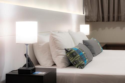 a white bed with pillows and a lamp on a table at Monreale Plus Midtown Campinas in Campinas