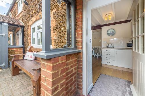 a brick wall in a kitchen with a wooden bench at Swift Cottage in Dersingham