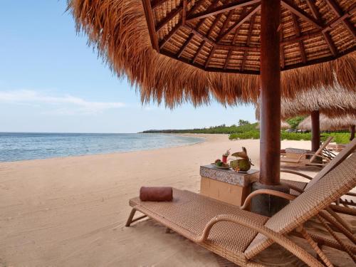 a beach with a straw umbrella and chairs and the ocean at The Grand Bali Nusa Dua in Nusa Dua