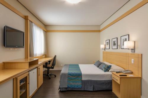 a hotel room with a bed and a desk and a tv at Monreale Plus Guarulhos International Airport in Guarulhos