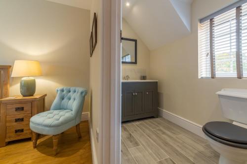 a bathroom with a toilet and a chair and a window at 1 Hall Lane Cottages in Thornham