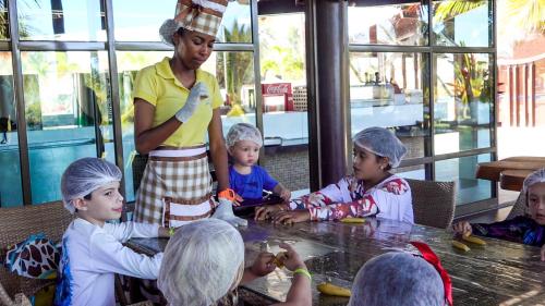 a group of children sitting around a table with a woman at Serrambi Resort in Porto De Galinhas