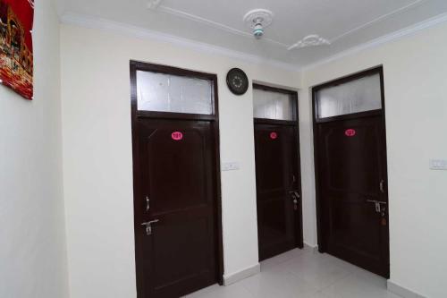 drie zwarte deuren in een kamer met een klok aan de muur bij Flagship Om Tara in McLeod Ganj