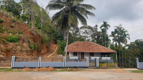 a small building with a fence and a palm tree at LAZY DAYS Wayanad in Cherambādi