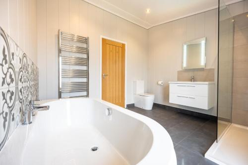 a white bathroom with a tub and a sink at Avocet Lodge in Ingoldisthorpe