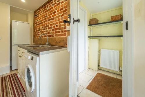 een keuken met een wasmachine en een bakstenen muur bij Margarets Cottage in Potter Heigham