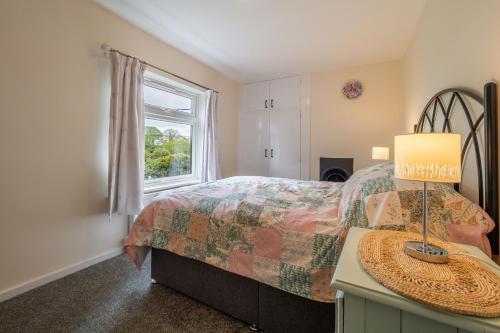 a bedroom with a bed with a lamp and a window at Margarets Cottage in Potter Heigham