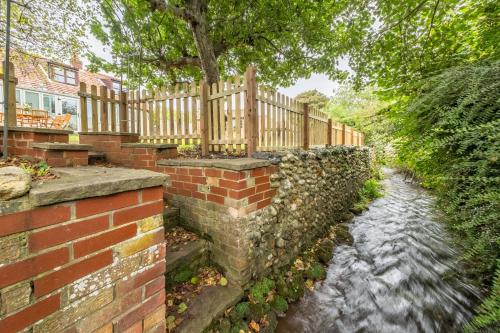 a brick wall next to a river with a fence at Evergreen in Thornage