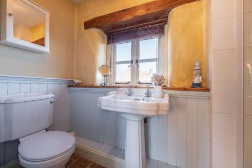 a bathroom with a toilet and a sink and a window at Church Cottage CA in Castle Acre