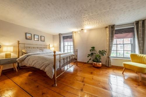 a bedroom with a bed and a chair and two windows at Teacup Cottage in Syderstone