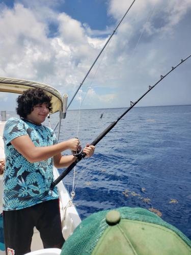 a man standing on a boat holding a fishing pole at El Padrino in Akumal