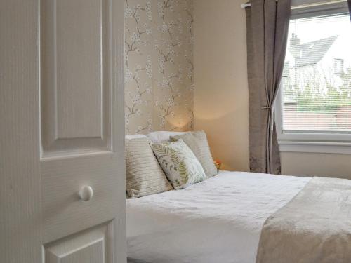 um quarto com uma cama branca e uma janela em Honeysuckle Cottage em Luncarty