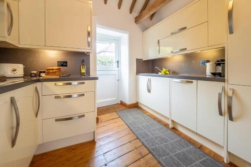 a kitchen with white cabinets and a wooden floor at The Stables in North Walsham
