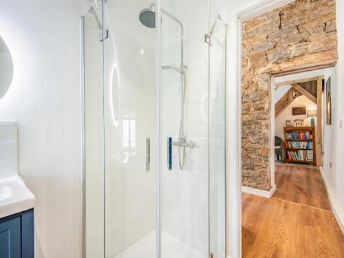 a glass shower in a bathroom with a stone wall at Jackdaw Cottage in Knighton