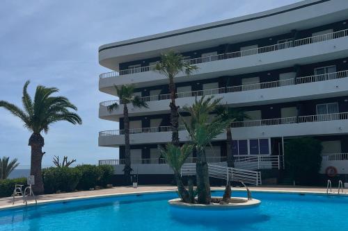 a swimming pool with palm trees in front of a building at Palmera Beach in Pilar de la Horadada