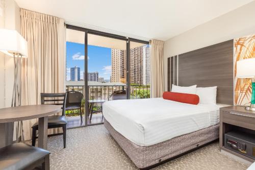 a hotel room with a bed and a desk and a balcony at CASTLE at Palms at Waikīkī in Honolulu