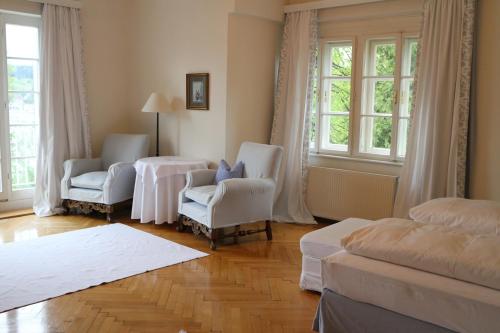 a bedroom with two chairs and a bed and windows at Hotel Seeschlößl Velden in Velden am Wörthersee