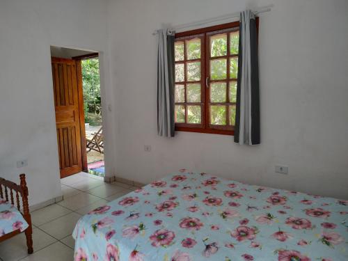 a bedroom with a bed with a floral bedspread and a window at Chalés Bela Vista in Paraty