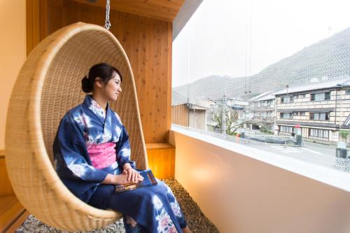 a woman sitting in a wicker chair on a balcony at UTSUROI Tsuchiya Annex in Toyooka