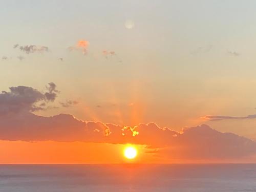 a sunset over the ocean with the sun hiding behind clouds at Gîtes Hotel Couleur Caraibes in Bouillante