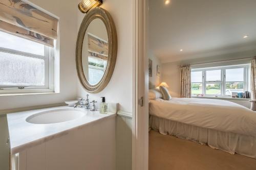 ein Bad mit einem Waschbecken, einem Bett und einem Spiegel in der Unterkunft Field Piece Cottage in Burnham Market