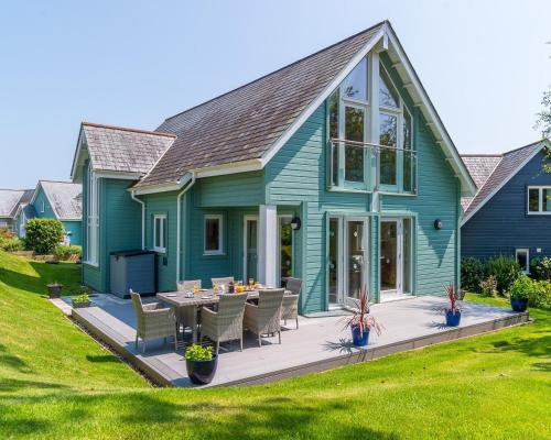 a blue house with a deck with a table and chairs at Trewhiddle Retreat V8 by Together Travel - Luxury 3-Bedroom Villa in St Austell