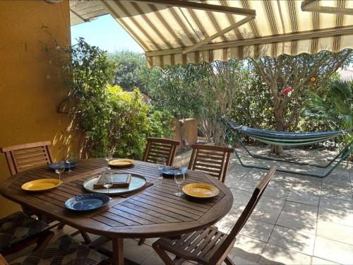 une table en bois avec des chaises et un hamac sur la terrasse. dans l'établissement Maison 3 pièces mezzanine, 7 couchages, piscine, proche plage à Saint Pierre la Mer - FR-1-229D-121, à Fleury