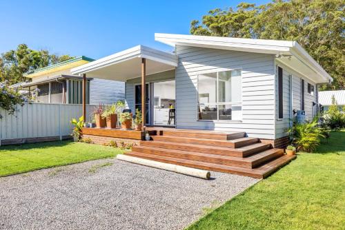 a small white house with a wooden staircase in a yard at Taylors Beach Cottage in Taylors Beach