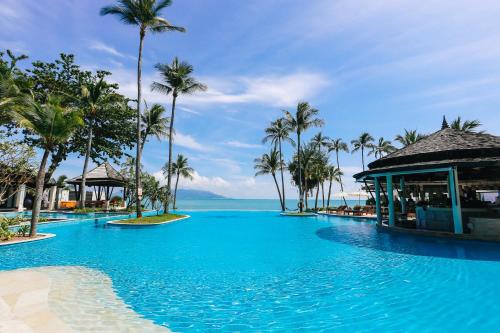 a large swimming pool with palm trees and the ocean at Melati Beach Resort & Spa - SHA Extra Plus Certified in Choeng Mon Beach