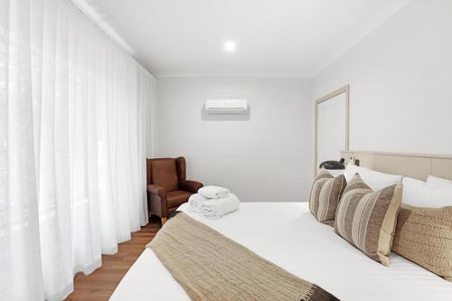 a white bedroom with a bed and a chair at Clare Country Club in Clare
